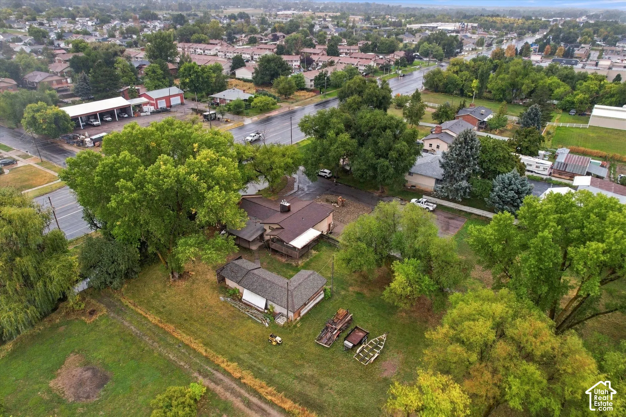 Aerial perspective featuring a multi-structure property on a expansive parcel with mature trees and asphalt paving