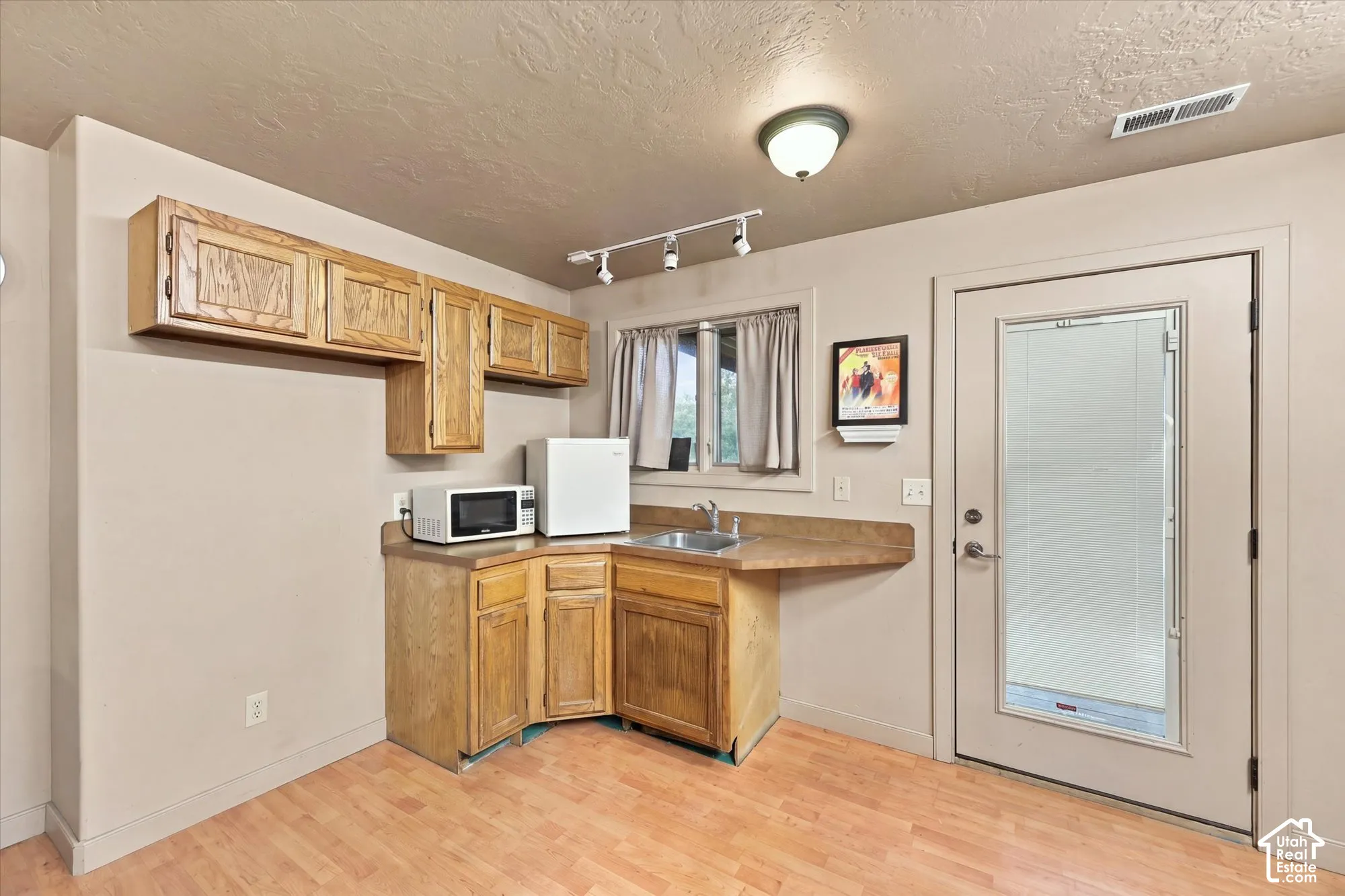 Kitchenette featuring wood-finish cabinetry, solid-surface countertops, a stainless steel sink, wood-finish flooring, and a glass-paneled exterior door