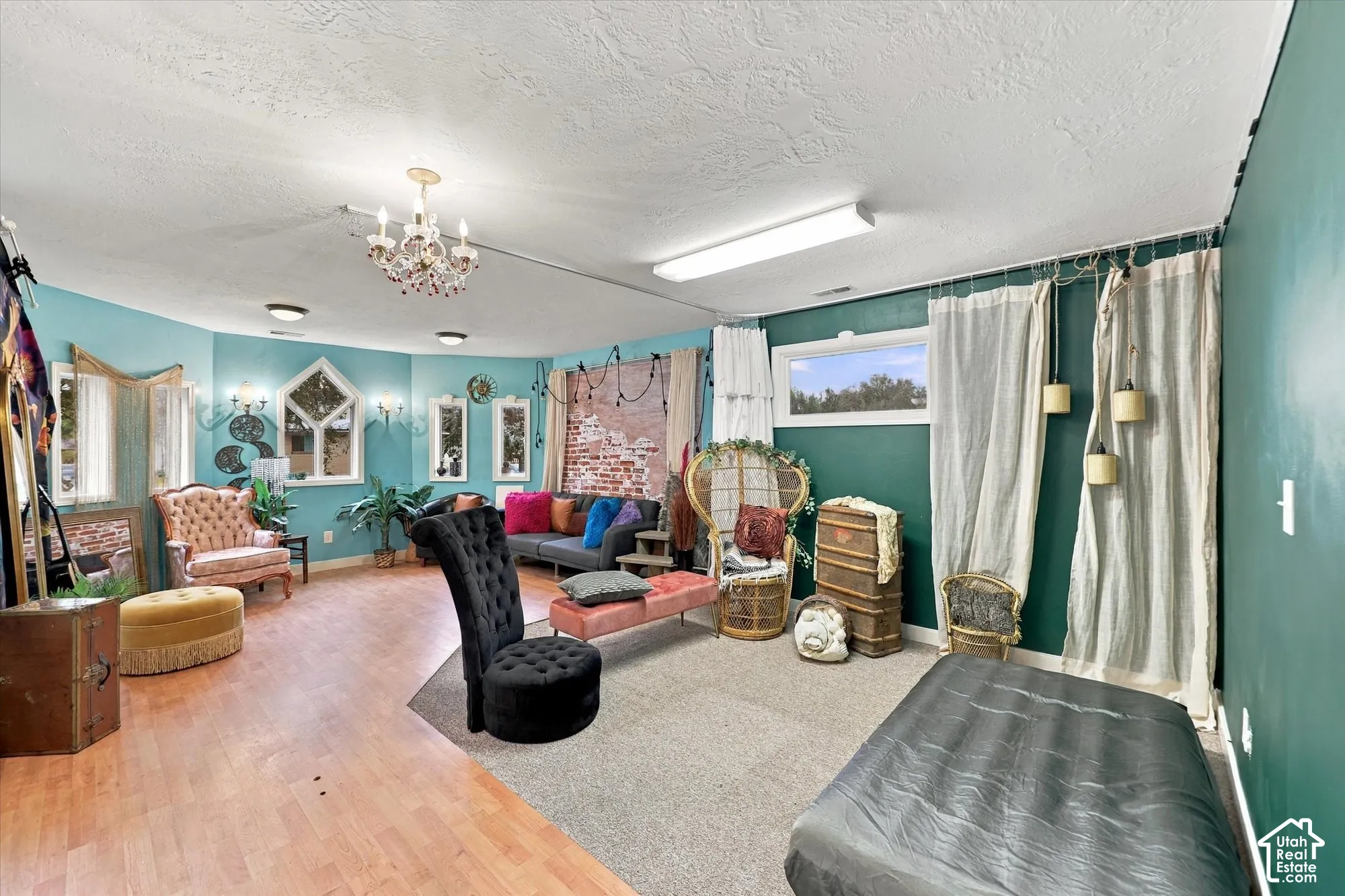 Expansive interior space featuring wood-finish flooring, exposed brick accent wall, ornate crystal chandelier, recessed lighting, and multiple windows