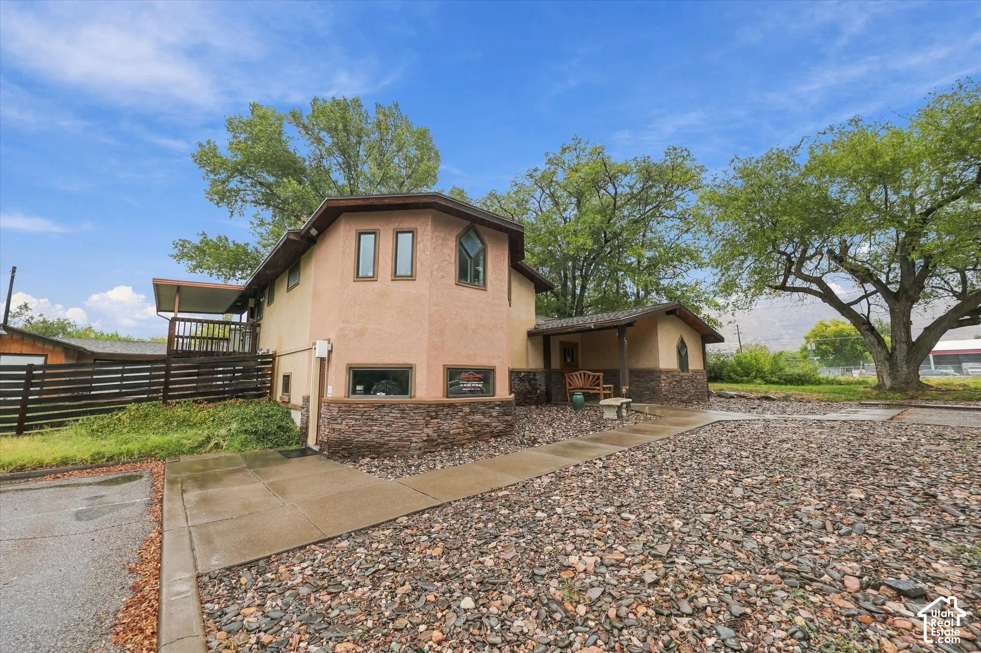 Exterior featuring a stucco facade with stacked stone veneer, a covered entrance, a raised balcony, and a gravel landscape