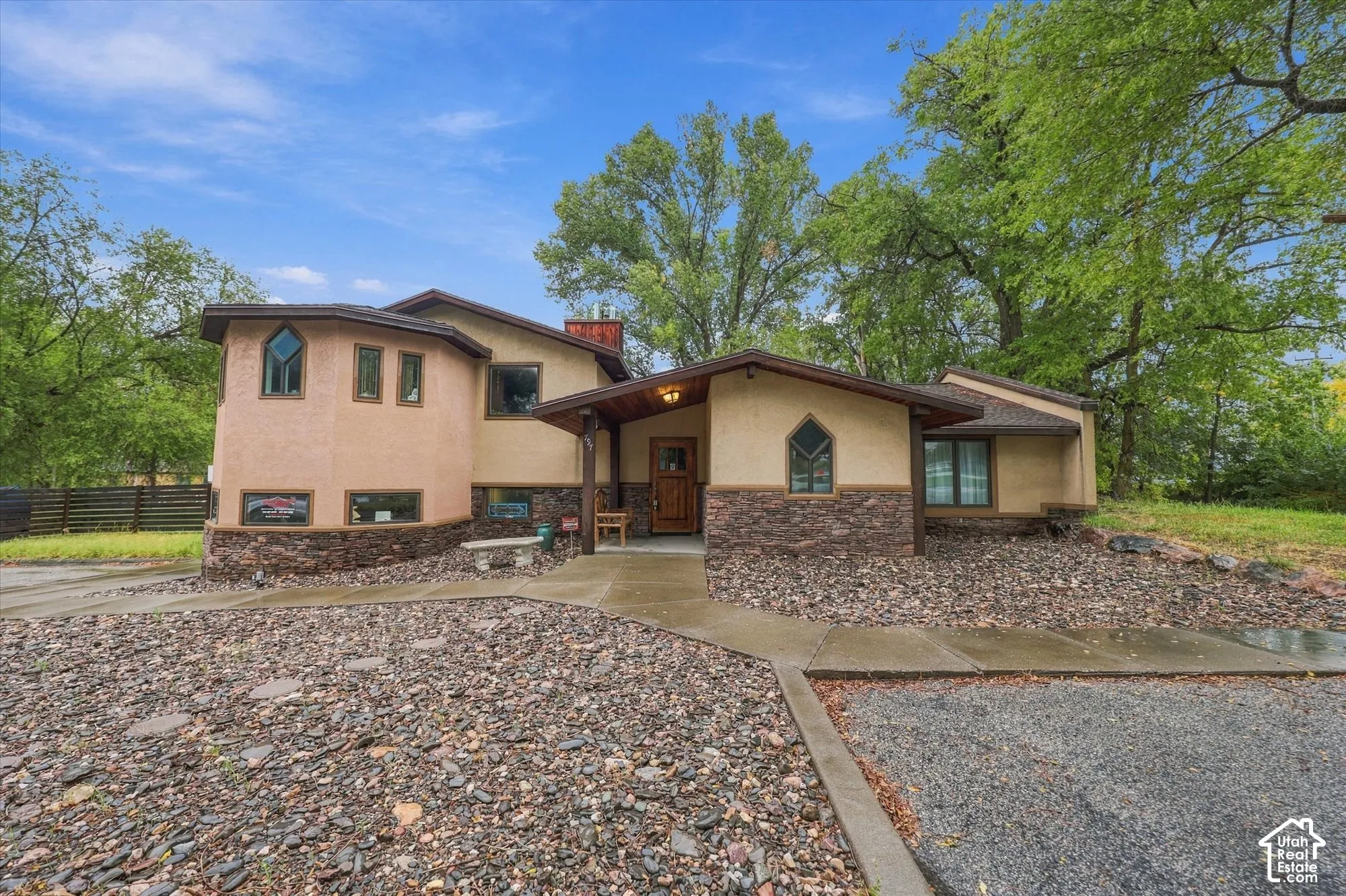 Stucco exterior featuring stacked stone accents, a covered front entryway, custom multi-pane windows, and rock-based landscaping