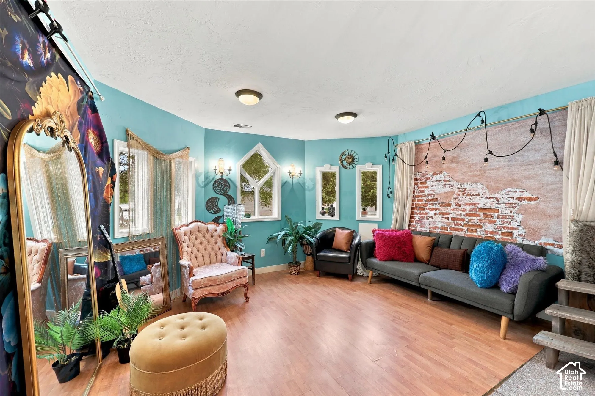 Living area featuring wood-finish flooring, exposed brick wall detailing, multiple windows with unique geometric framing, and wall-mounted sconces