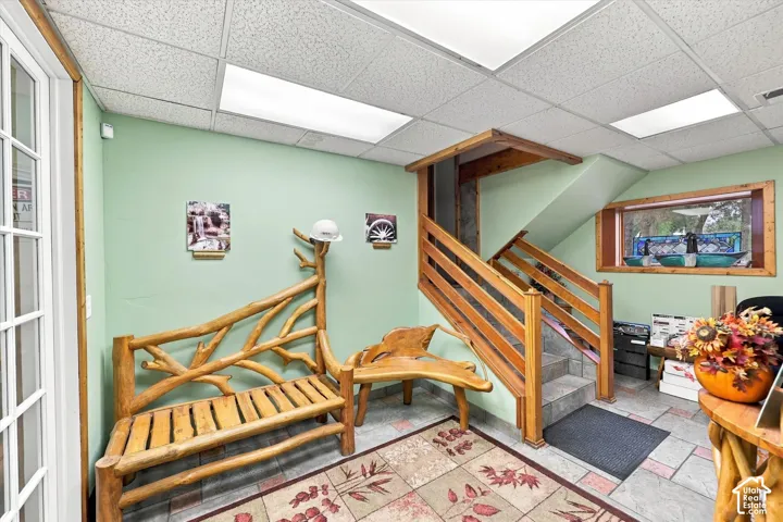 Interior space featuring stone tile flooring, a staircase with wood railings, recessed panel ceiling lights, and wooden window trim