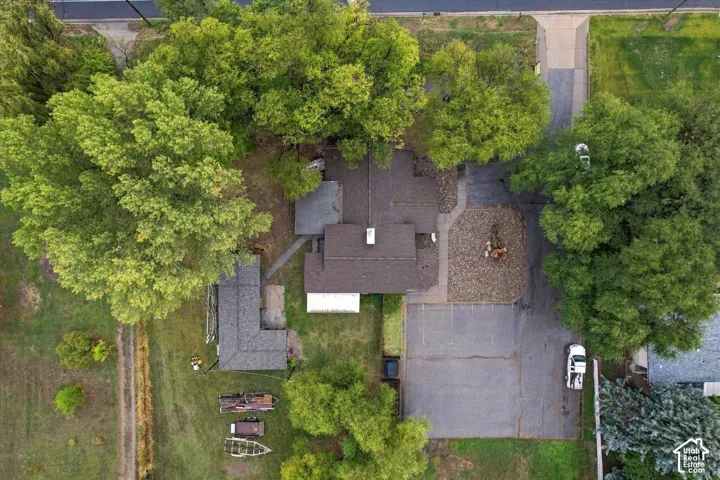 Aerial perspective of property featuring mature tree canopy, extensive asphalt driveway, aggregate surfacing, and multiple structure footprints