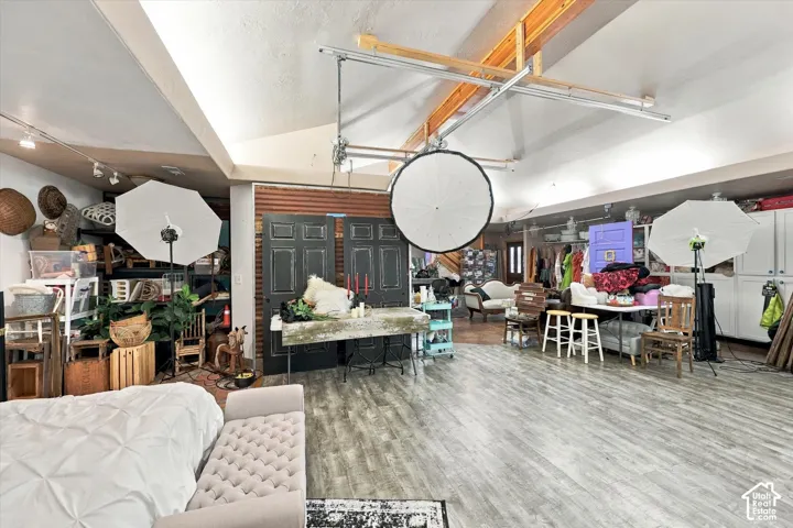 Vaulted ceilings with exposed timber beams, wood-finish flooring, track lighting, and built-in white cabinetry