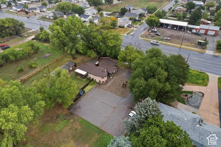 Aerial perspective of a detached property featuring an expansive asphalt parking area, a stone-surfaced courtyard, a covered porch, and mature trees on a spacious lot