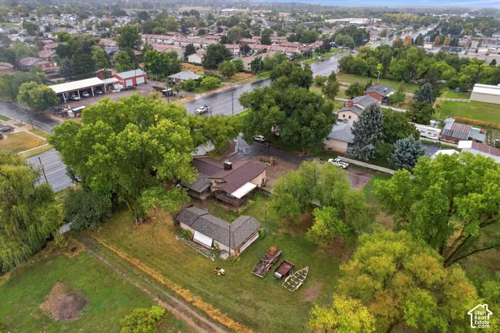 Aerial perspective featuring a multi-structure property on a expansive parcel with mature trees and asphalt paving