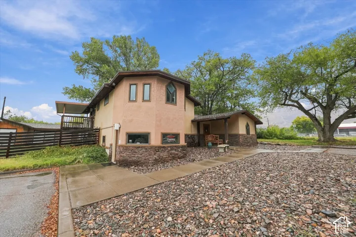 Exterior featuring a stucco facade with stacked stone veneer, a covered entrance, a raised balcony, and a gravel landscape