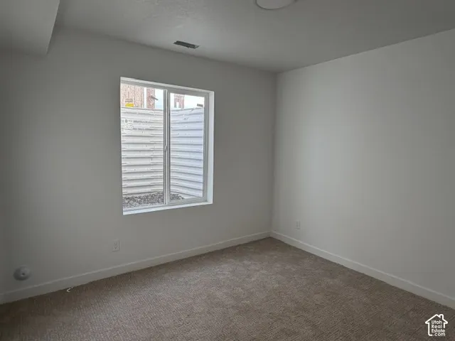 Neutral-toned interior space featuring light-colored wall paint, plush carpeting, and a recessed window well with a corrugated metal surround