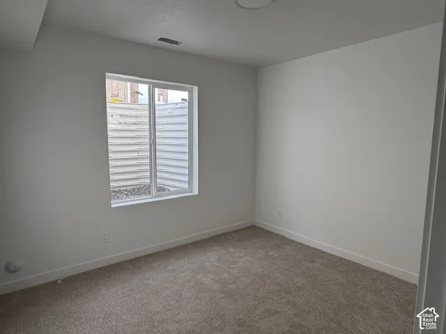 Neutral-toned interior room featuring wall-to-wall carpeting and a window with a window well