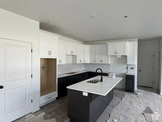 Kitchen featuring white upper cabinetry, dark base cabinetry, a central island with a stone-finish countertop, undermount sink, and matte black hardware