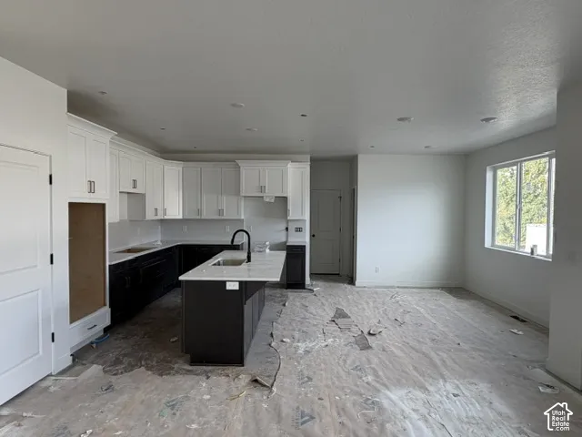 Kitchen featuring white upper cabinetry, dark lower cabinetry, quartz countertops, a center island, and a matte black faucet
