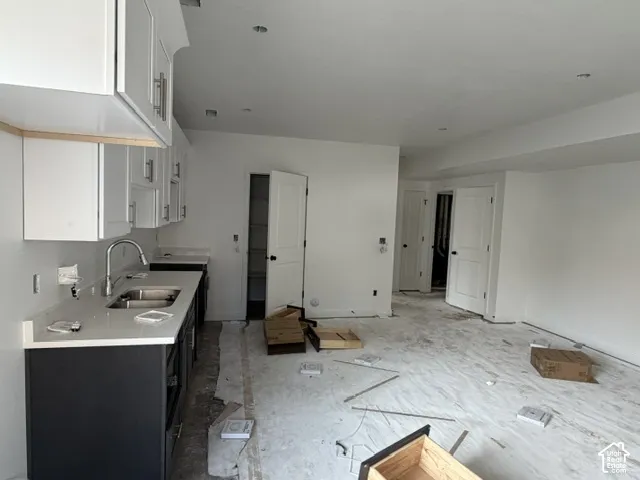 Kitchen featuring white upper cabinetry, dark base cabinetry, light-toned stone-finish countertops, stainless steel dual-basin sink with arched faucet, and built-in pantry