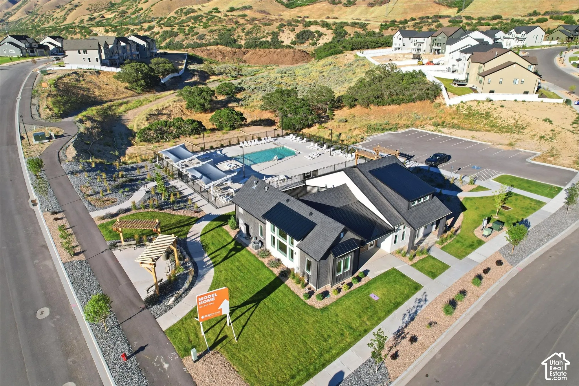 Aerial perspective of community facilities featuring a swimming pool, paved parking area, wooden pergola structures, and manicured lawn spaces
