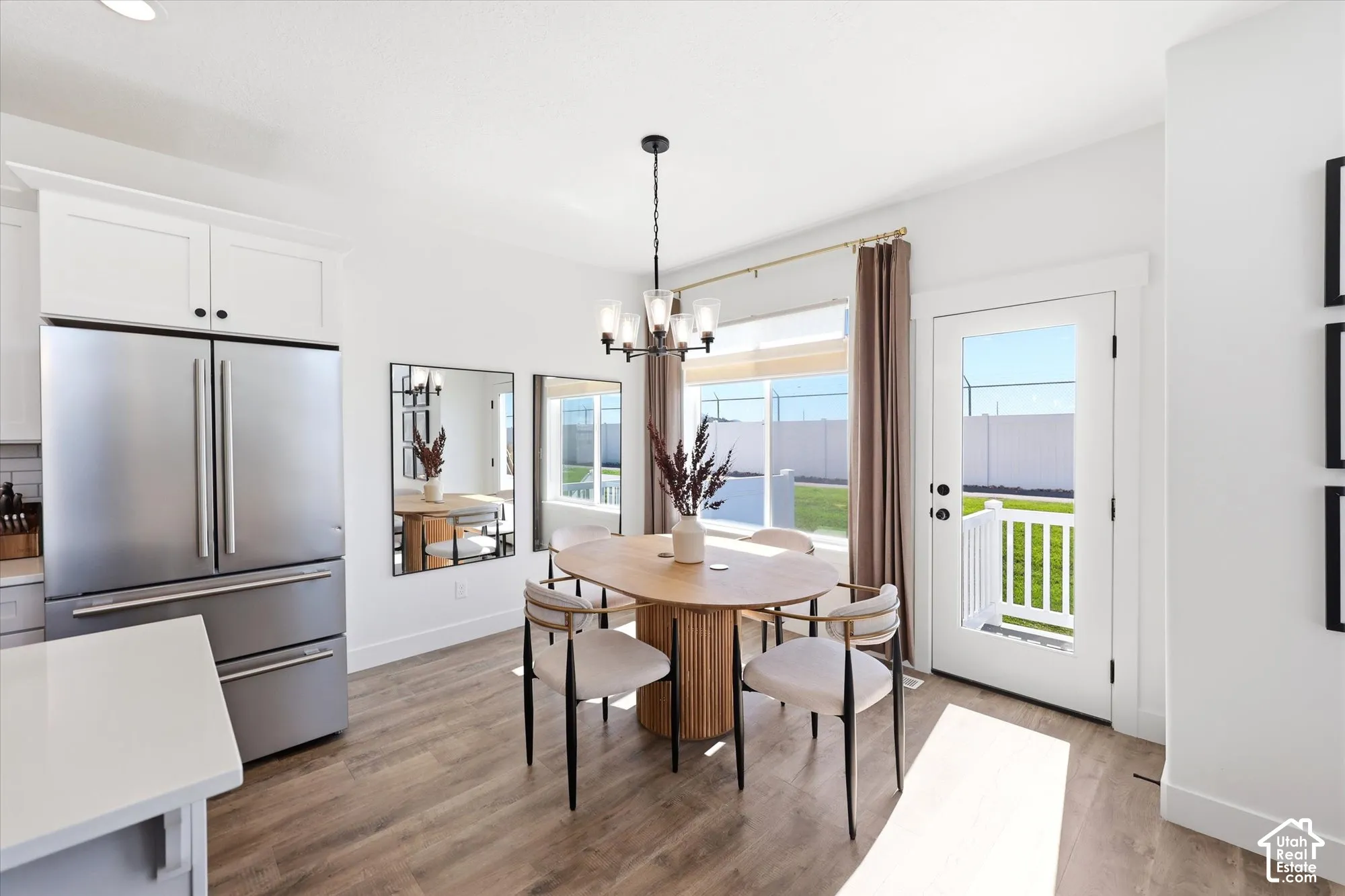 Kitchen featuring white cabinetry, stainless steel refrigerator, wood-finish flooring, multi-light chandelier, and a glass-paneled exterior door