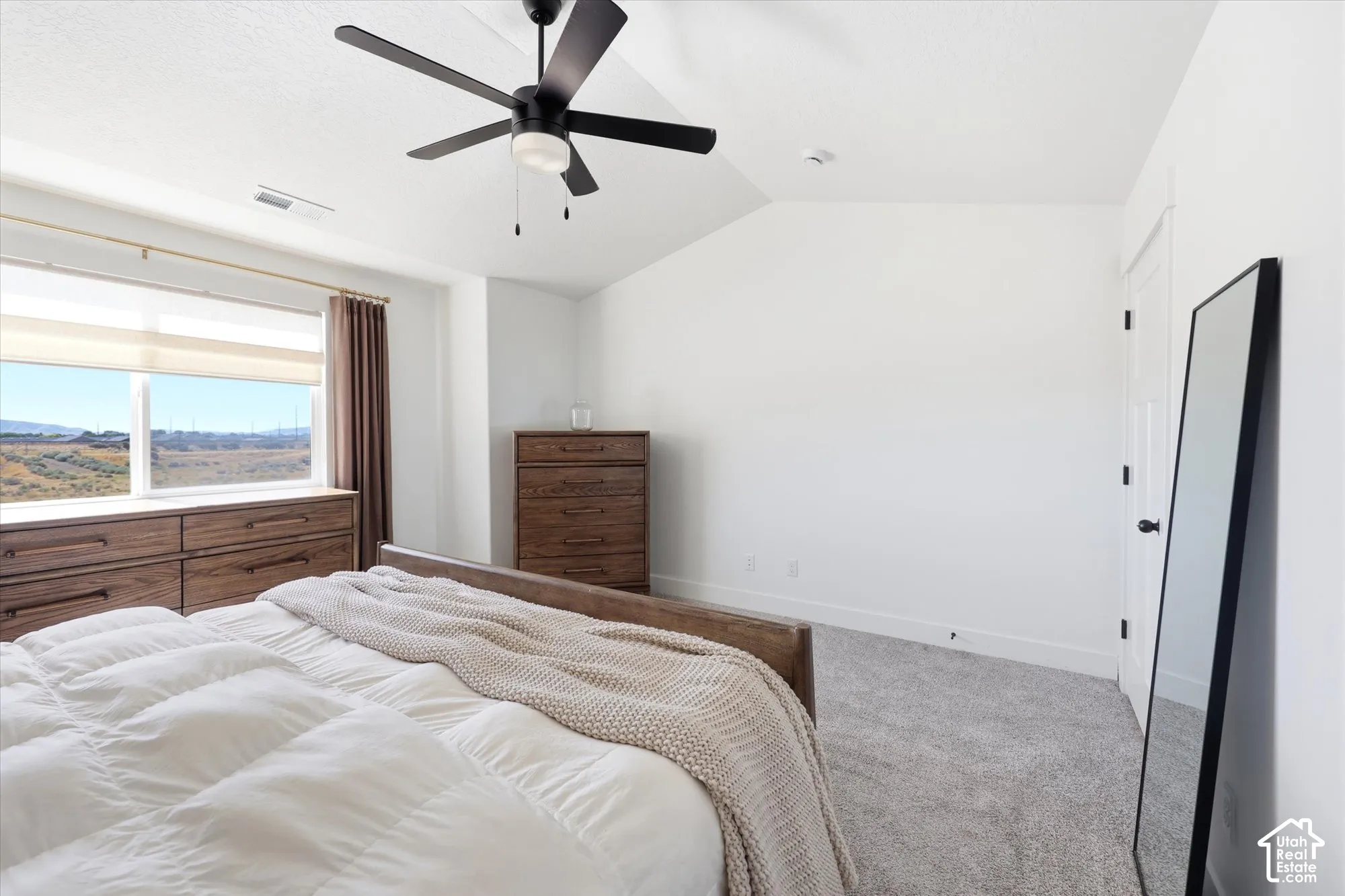 Vaulted ceilings, neutral carpeting, and a matte black ceiling fan with integrated lighting