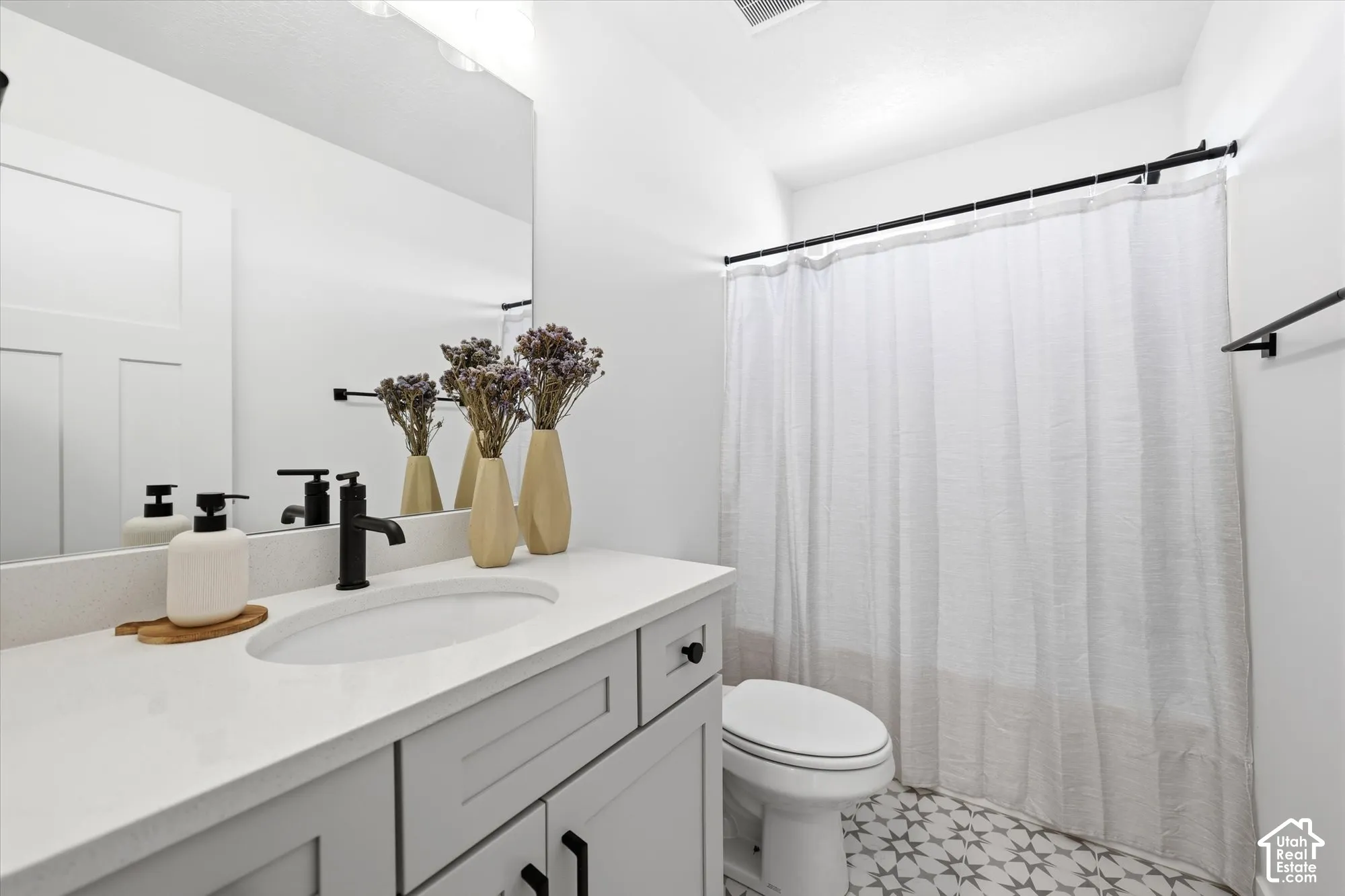 Light gray vanity with a solid-surface countertop, oval undermount sink, matte black faucet hardware, and patterned geometric floor tile