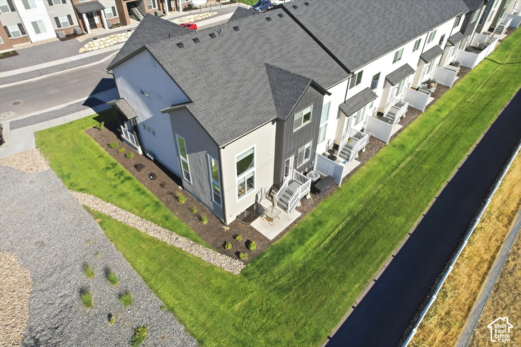 Multi-level townhome featuring a mixed-material exterior, shingled roofing, concrete patio, and landscaping with mulch beds