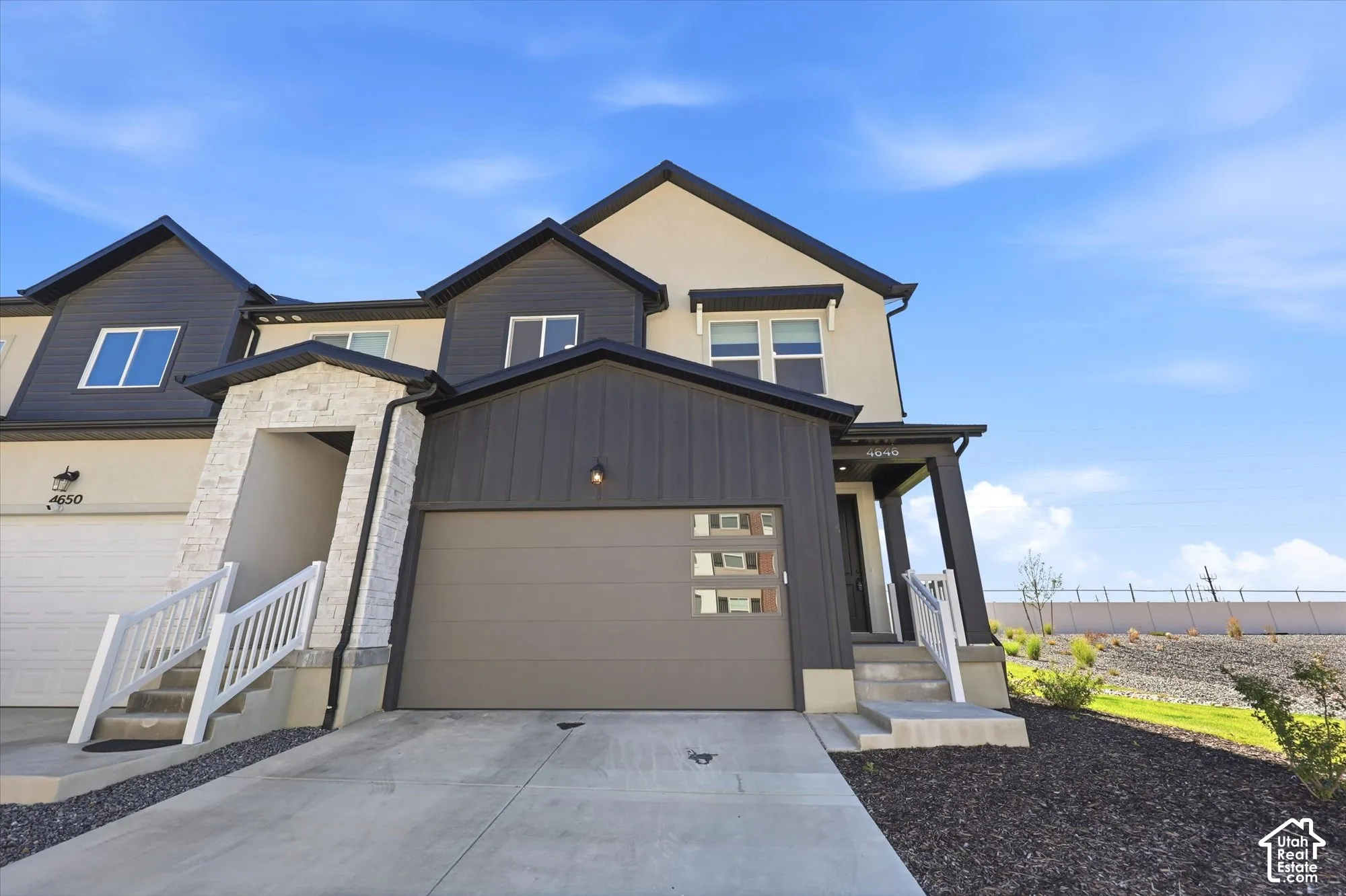 Exterior featuring a mixed-material facade of stucco and vertical metal siding, stone veneer accents, an attached garage with horizontal glass paneling, and concrete entry steps with white railing