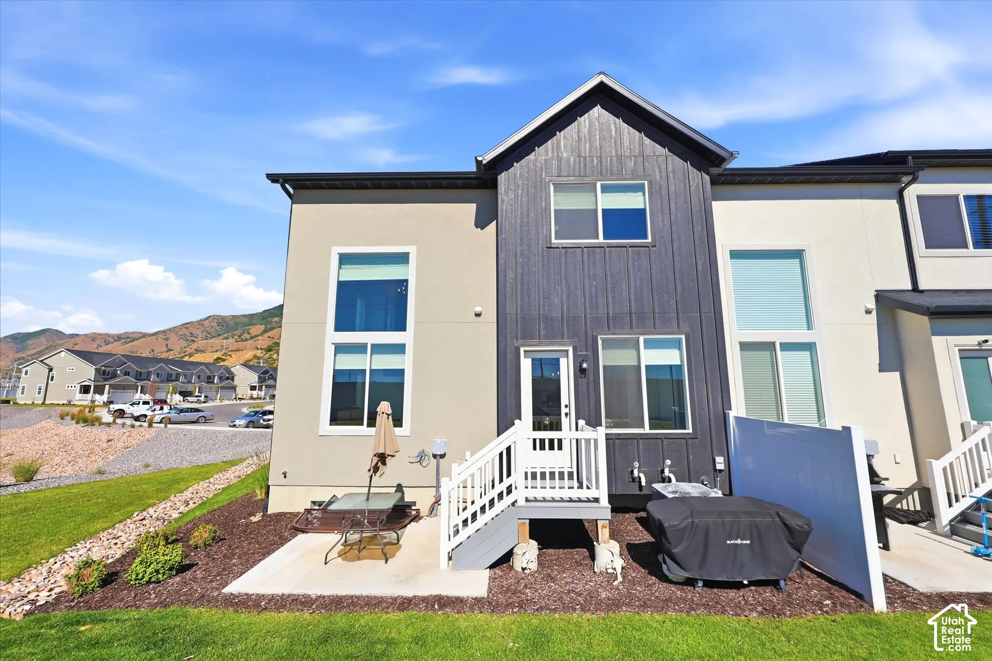 Exterior featuring a combination of stucco and vertical wood-finish siding, tall windows, a private concrete patio, and a white vinyl privacy screen