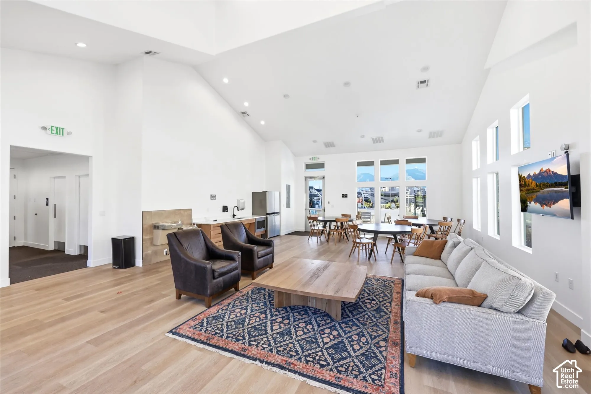 Vaulted ceilings, wood-finish flooring, recessed lighting, expansive multi-pane windows, and a built-in kitchenette featuring tile backsplash and stone-finish countertops