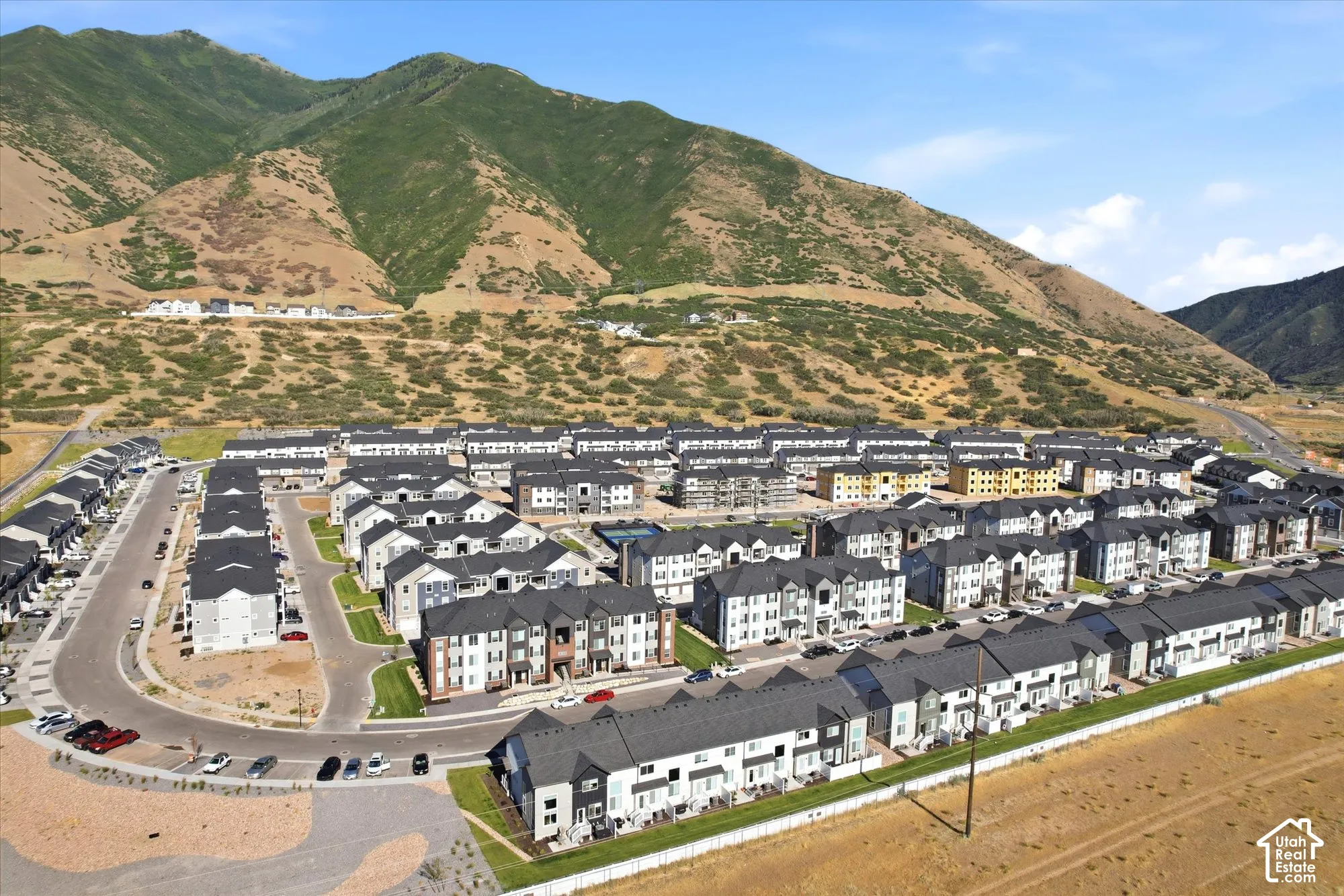 Aerial perspective of a multi-unit residential community featuring multi-story structures with pitched roofs, situated at the base of a mountain range