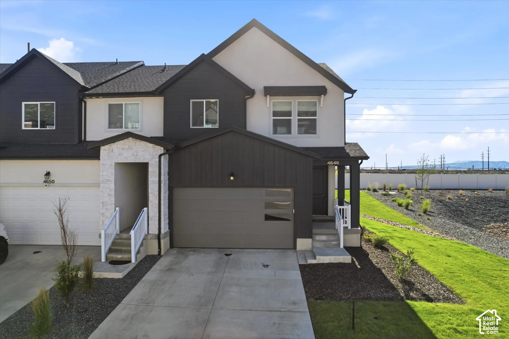 Multi-level townhome exterior featuring high-contrast vertical siding, textured stone masonry detailing, a two-car garage with modern horizontal window accents, and a concrete driveway
