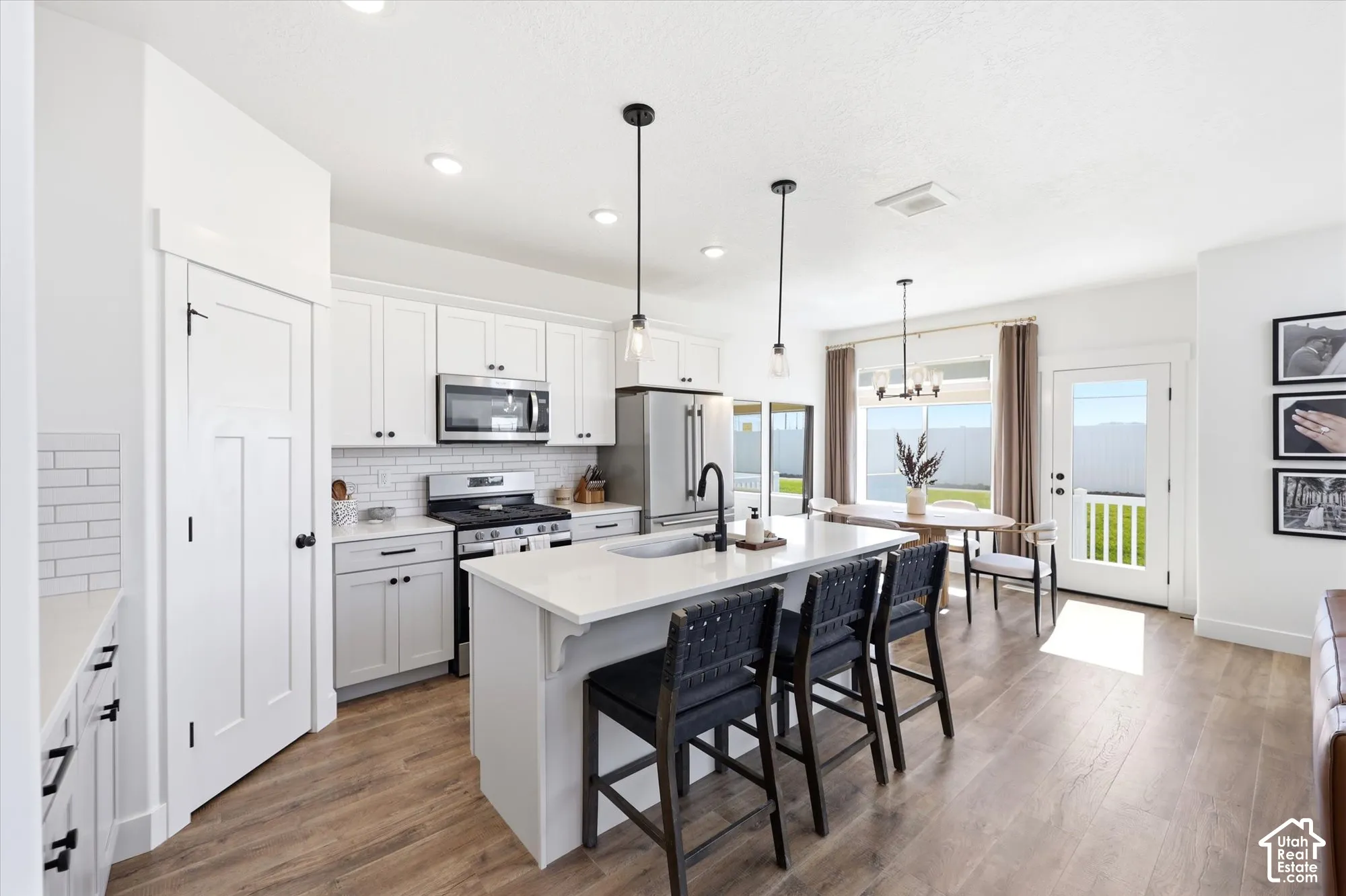 Kitchen featuring white shaker-style cabinetry, quartz countertops, a central island with a matte black faucet, subway tile backsplash, and wood-finish flooring