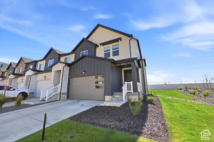 Multi-level townhome exterior featuring vertical board-and-batten siding, stone veneer accents, an attached two-car garage, and a covered front entryway with white railings