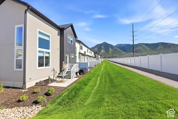 Modern multi-family exterior featuring concrete and vertical metal siding, rear patio access, manicured green space, and mountain backdrop