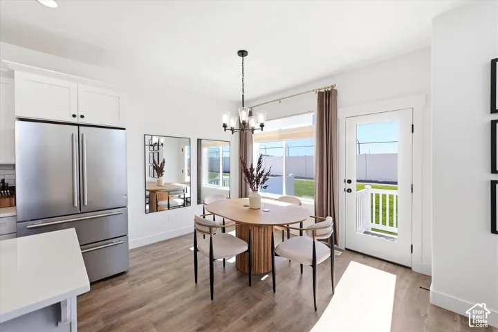 Kitchen featuring white cabinetry, stainless steel refrigerator, wood-finish flooring, multi-light chandelier, and a glass-paneled exterior door