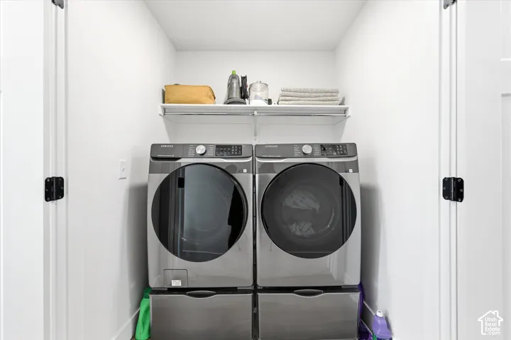 Laundry closet featuring side-by-side metallic-finish appliances on elevated pedestals with an integrated overhead wire storage shelf and double-door enclosure