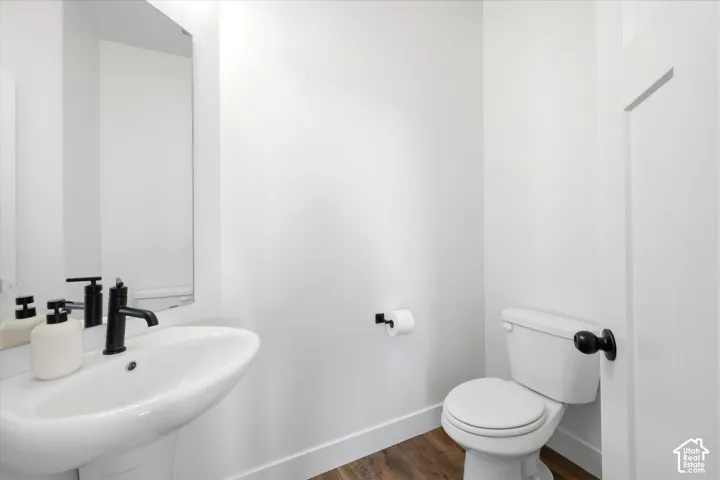 Powder room featuring a pedestal sink, matte black faucet, wall-mounted mirror, and wood-finish flooring
