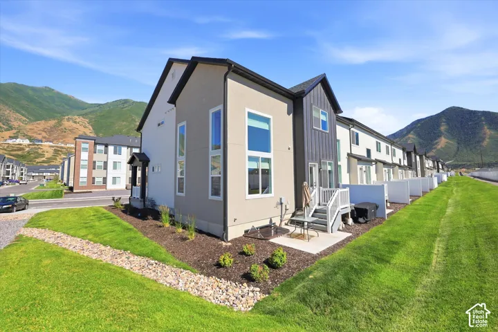 Modern multi-story exterior featuring a mix of stucco and vertical metal siding, tall oversized windows, a concrete patio, and a mountain backdrop