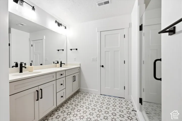 Dual-sink vanity with matte black fixtures, quartz countertop, patterned tile flooring, and glass-enclosed shower with matte black hardware