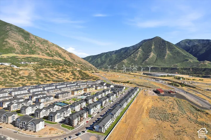 Aerial perspective of a multi-building residential development featuring mountain scenery, paved streets, exterior parking areas, and on-site recreational courts