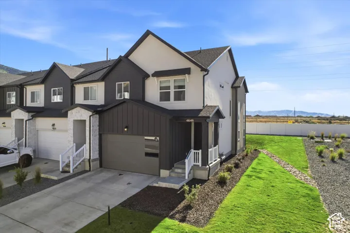 Multi-level exterior featuring a combination of vertical board-and-batten siding and stone masonry, a composite shingle roof, an attached garage, and a concrete driveway