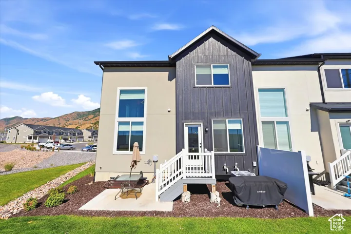 Exterior featuring a combination of stucco and vertical wood-finish siding, tall windows, a private concrete patio, and a white vinyl privacy screen