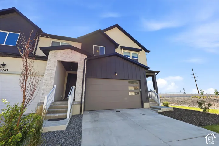 Multi-level exterior featuring vertical siding, stucco finish, stone-clad entryway, and a garage door with integrated glass panels