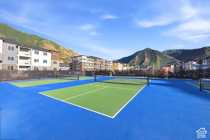 Multi-court hardscape recreation area featuring blue and green synthetic surfacing, black chain-link perimeter fencing, and mountain backdrop