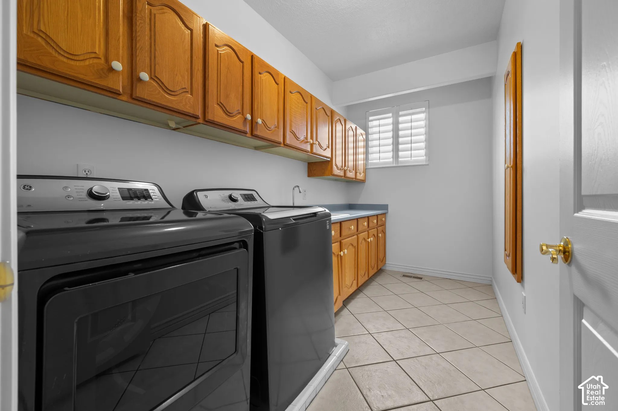 Laundry room with tile flooring, a sink, and plantation-style window shutters