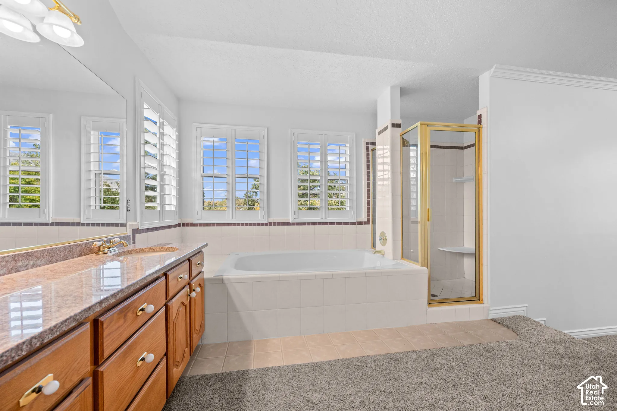 Primary bathroom featuring a tiled soaking tub, a glass-enclosed shower, and window shutters