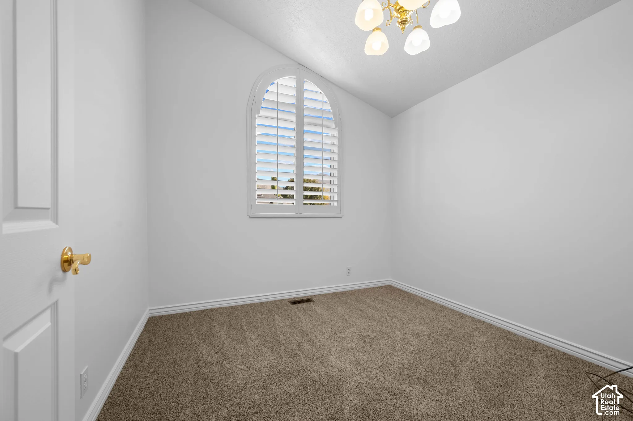 Bedroom with an arched window with plantation shutters, neutral carpeting, and a multi-light ceiling fan