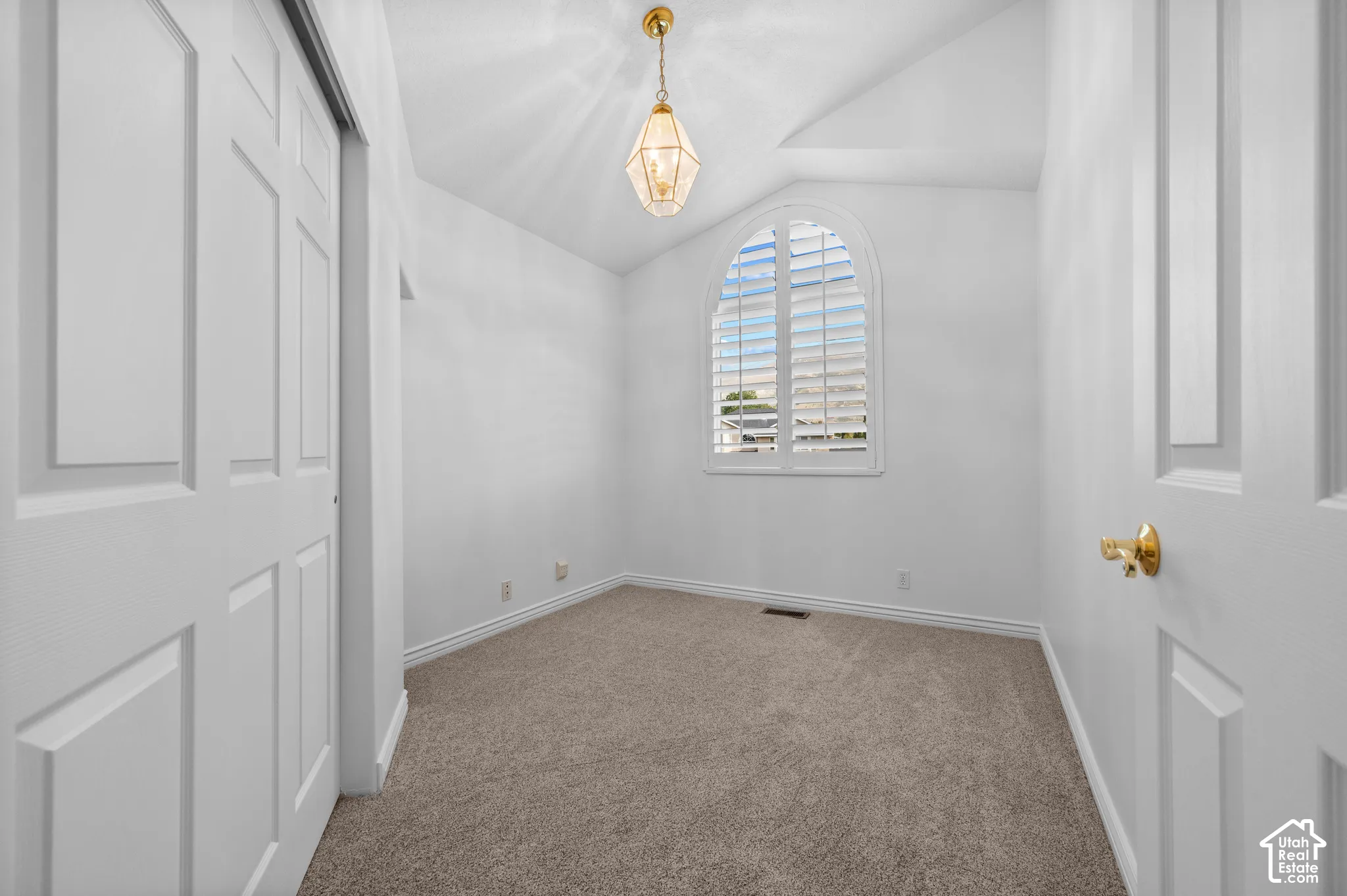 Bedroom featuring vaulted ceiling, an arched window with plantation shutters, neutral carpeting, and a pendant light fixture