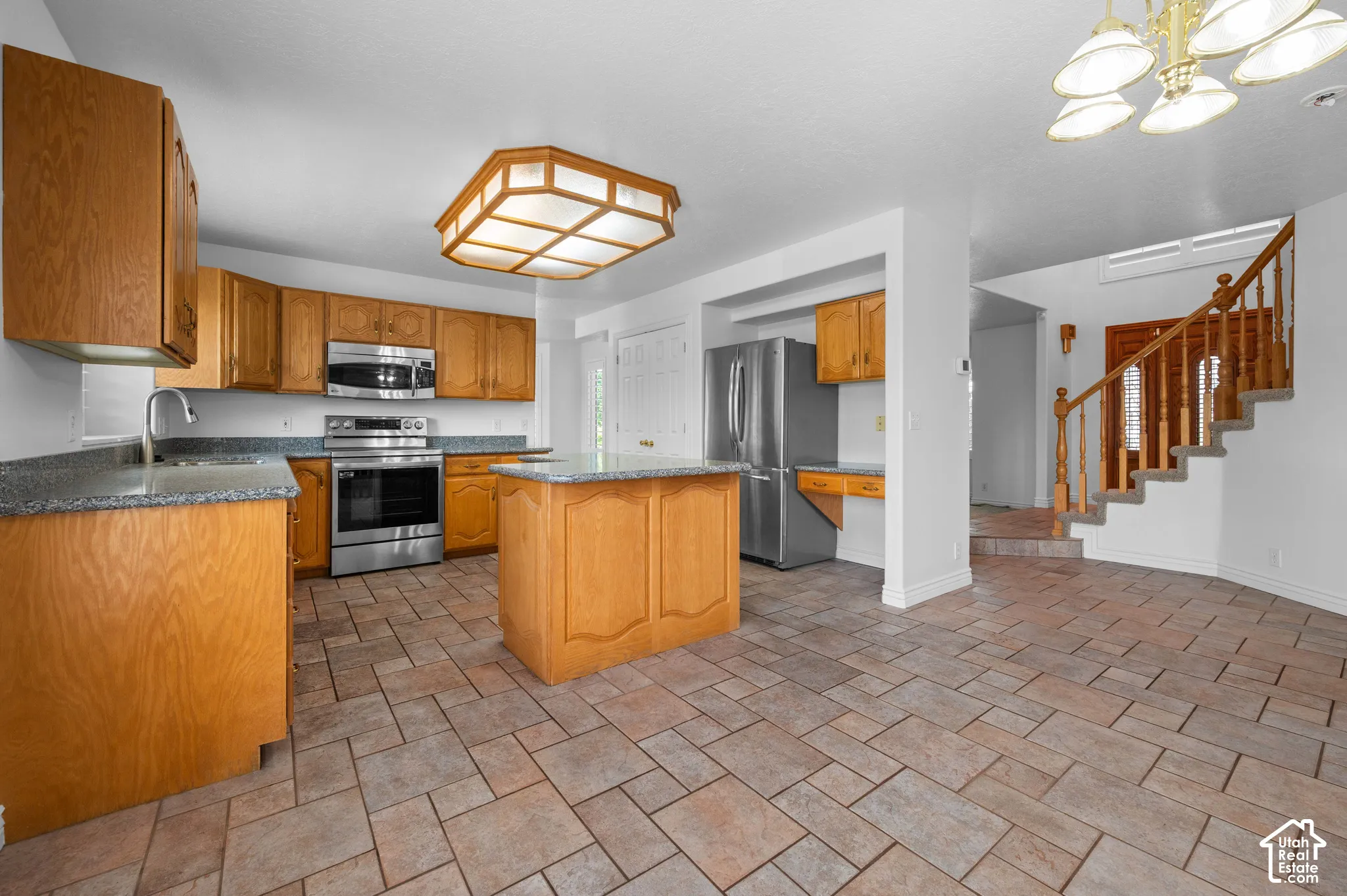 Kitchen featuring wood cabinetry, granite countertops, central island, stainless steel appliances, and tile flooring