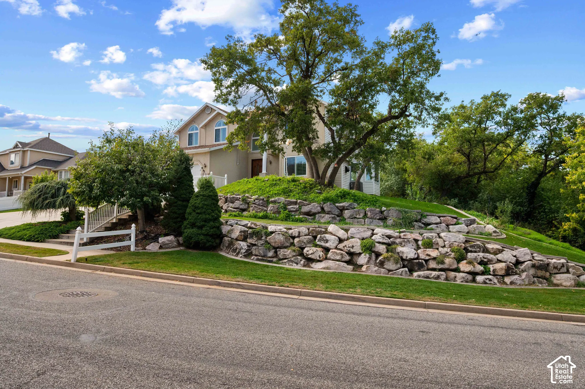 View of front of house featuring natural stone tiered retaining walls, and mature trees