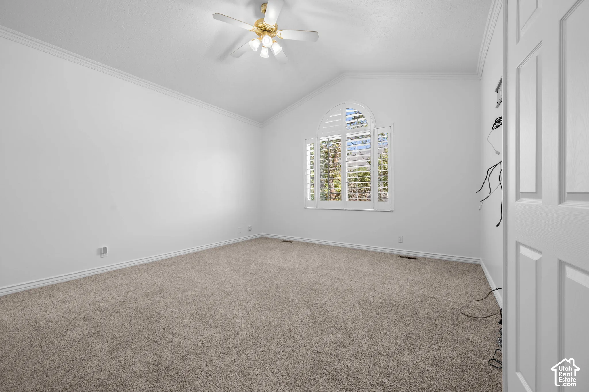 Primary Bedroom with vaulted ceilings, arched window with plantation shutters, neutral carpeting, and a multi-light ceiling fan