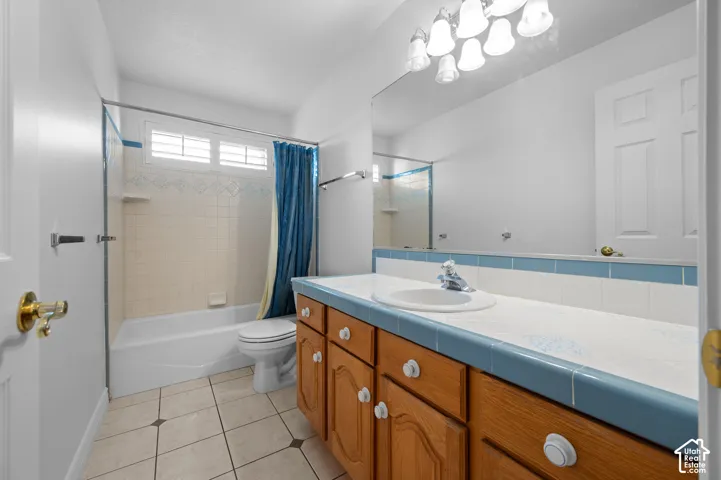 Bathroom featuring a vanity with tile countertop, a large wall-mounted mirror, multi-light fixture, and tile flooring
