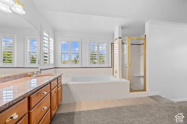 Primary bathroom featuring a tiled soaking tub, a glass-enclosed shower, and window shutters