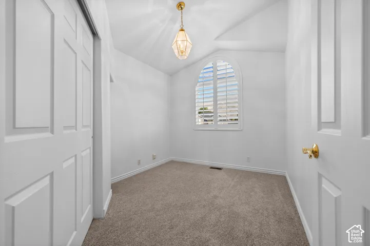 Bedroom featuring vaulted ceiling, an arched window with plantation shutters, neutral carpeting, and a pendant light fixture